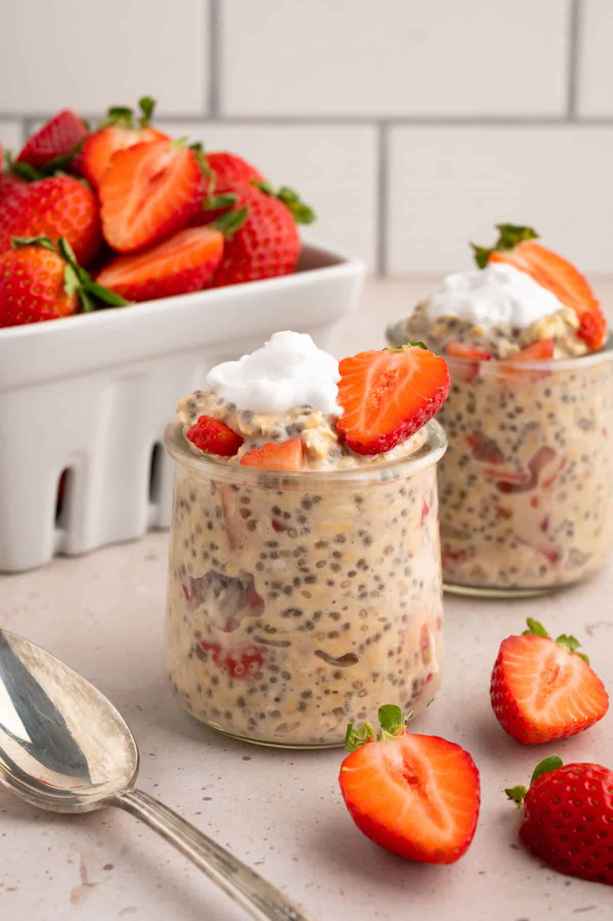 Strawberries and cream overnight oats in glass jars with strawberries in the background.