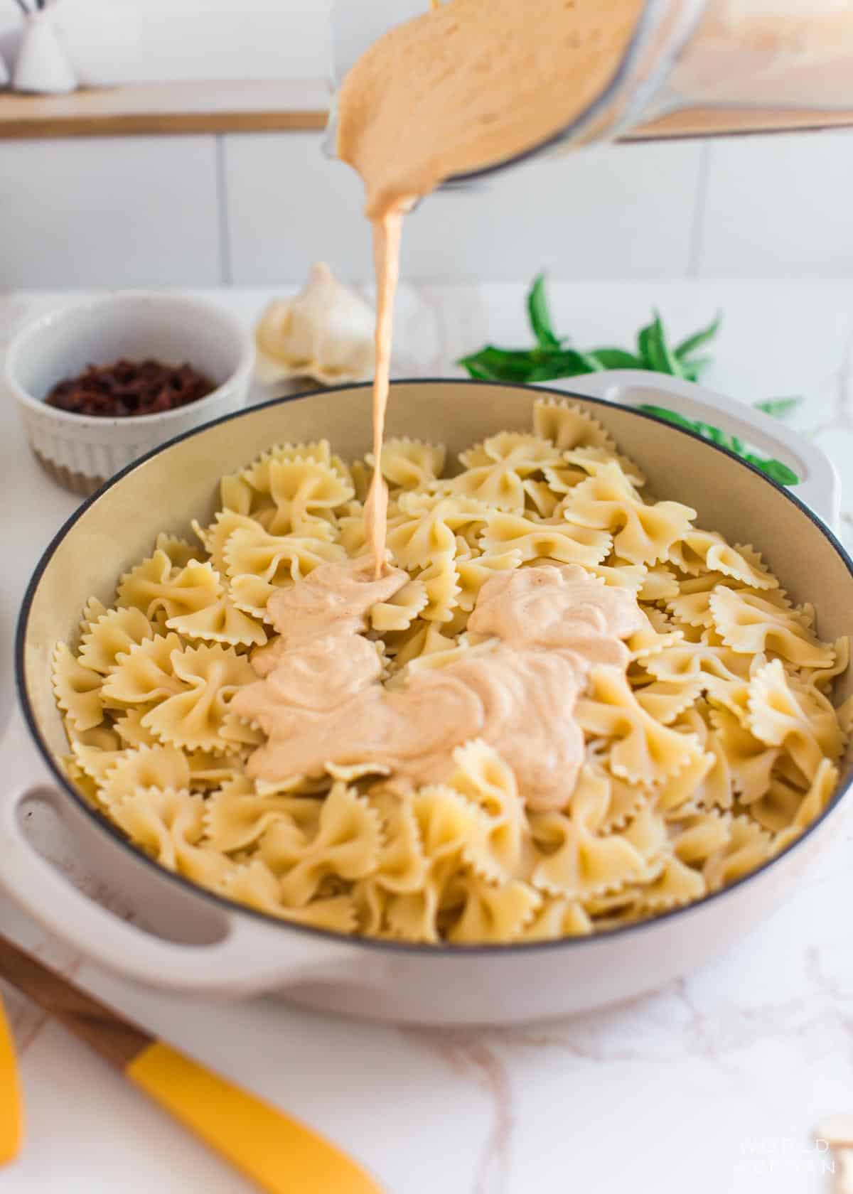 Sun-dried tomato sauce pouring onto cooked pasta from a blender pitcher.