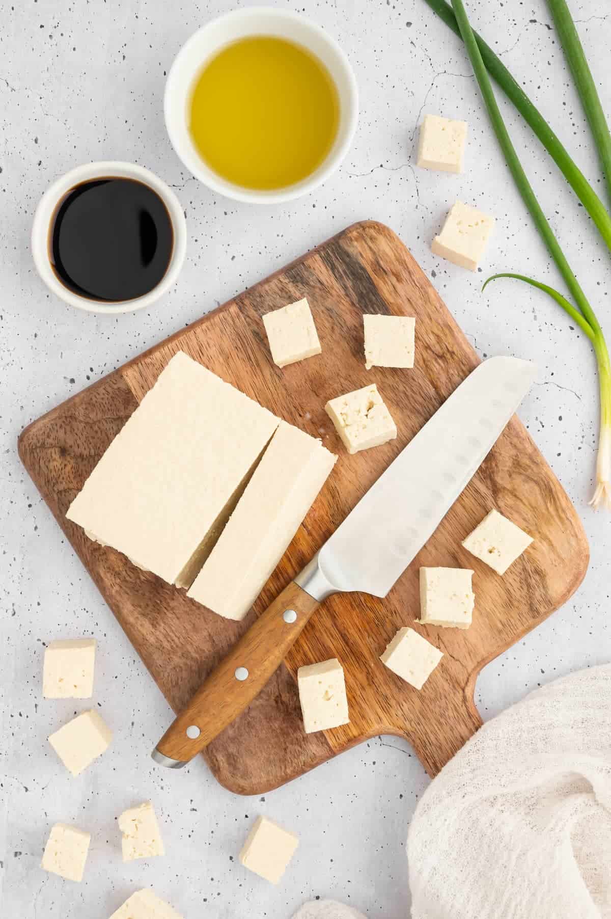 Tofu cut and cubed on a wooden cutting board.