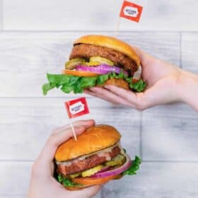 Hands holding out vegan Beyond Meat burgers with flags.