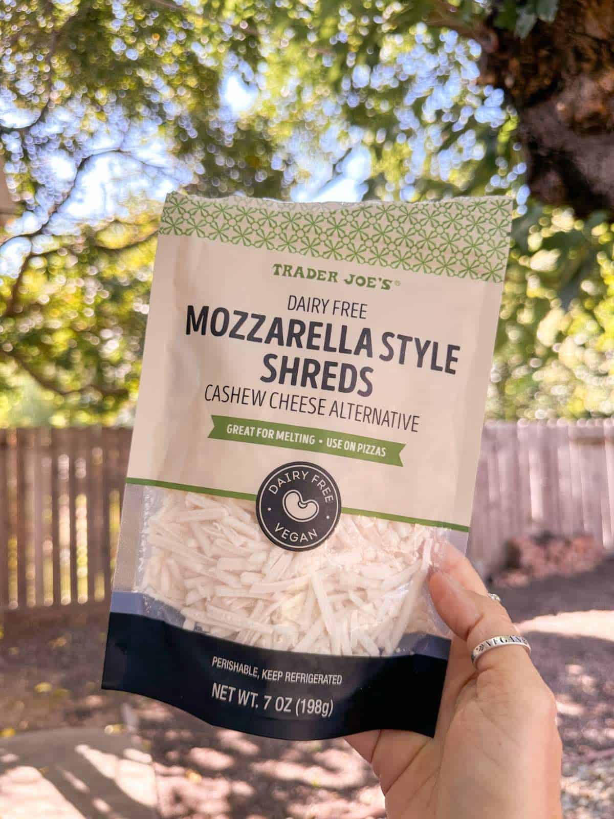 Woman holding out a package of vegan mozzarella shreds from the grocery store Trader Joe's.