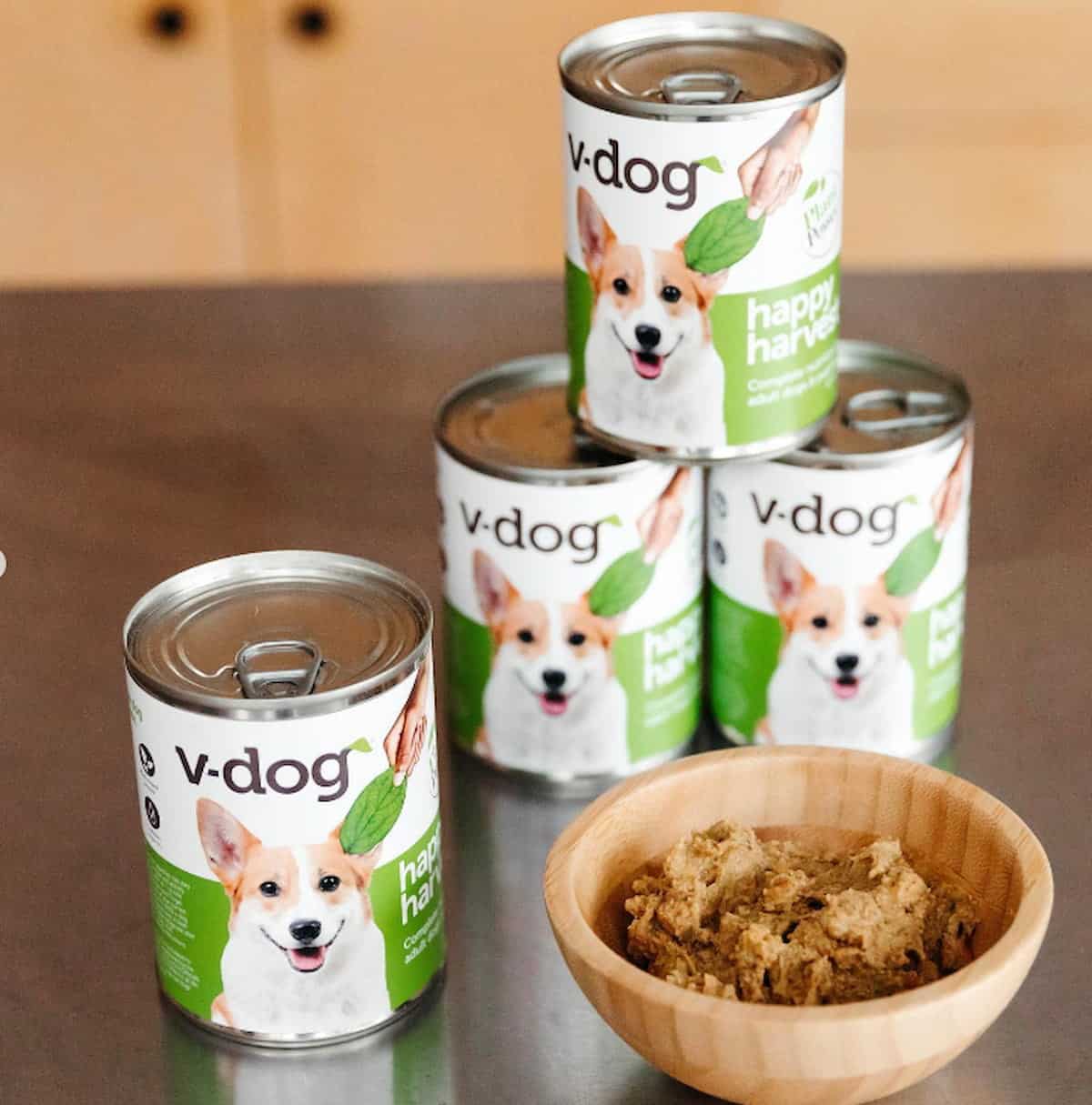 Cans of V-Dog's Happy Harvest dog food next to a bowl of it.