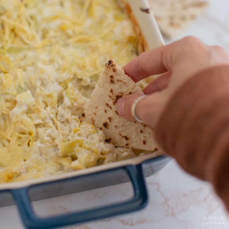 creamy vegan artichoke dip being scooped up with a piece of pita bread