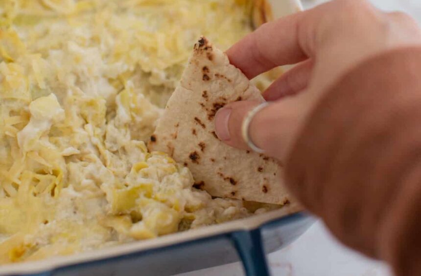 creamy vegan artichoke dip being scooped up with a piece of pita bread