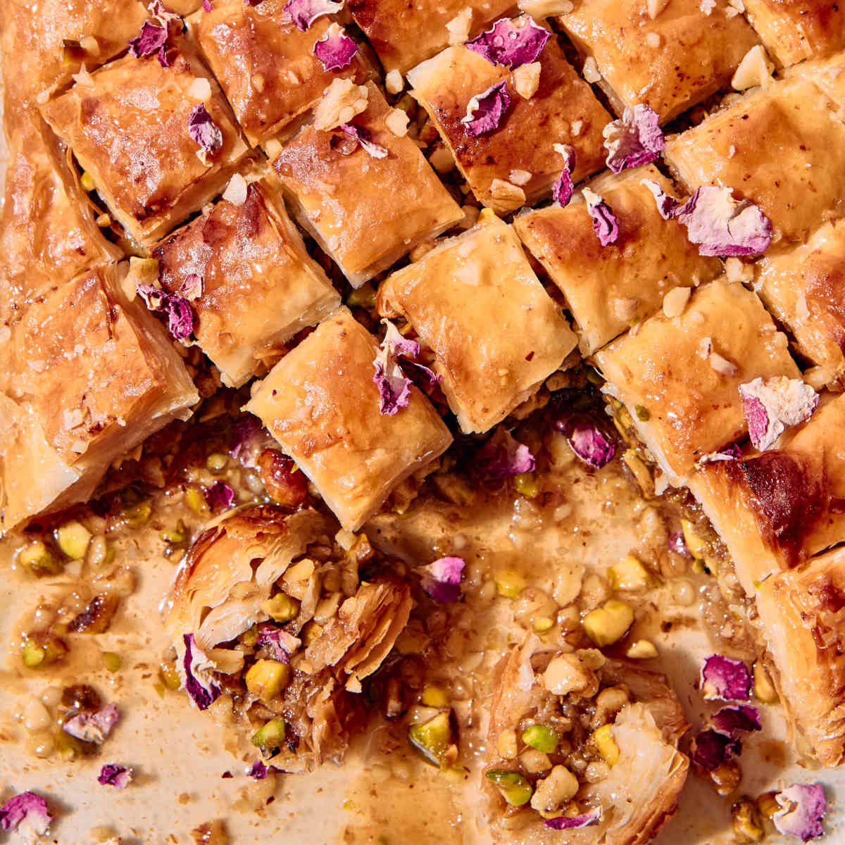 Vegan baklava on a baking tray, sliced diagonally into diamond shapes with rose petals on top.