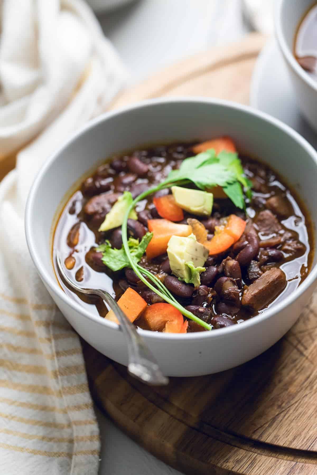 A bowl of vegan black bean soup garnished with diced tomato, avocado, and fresh cilantro.