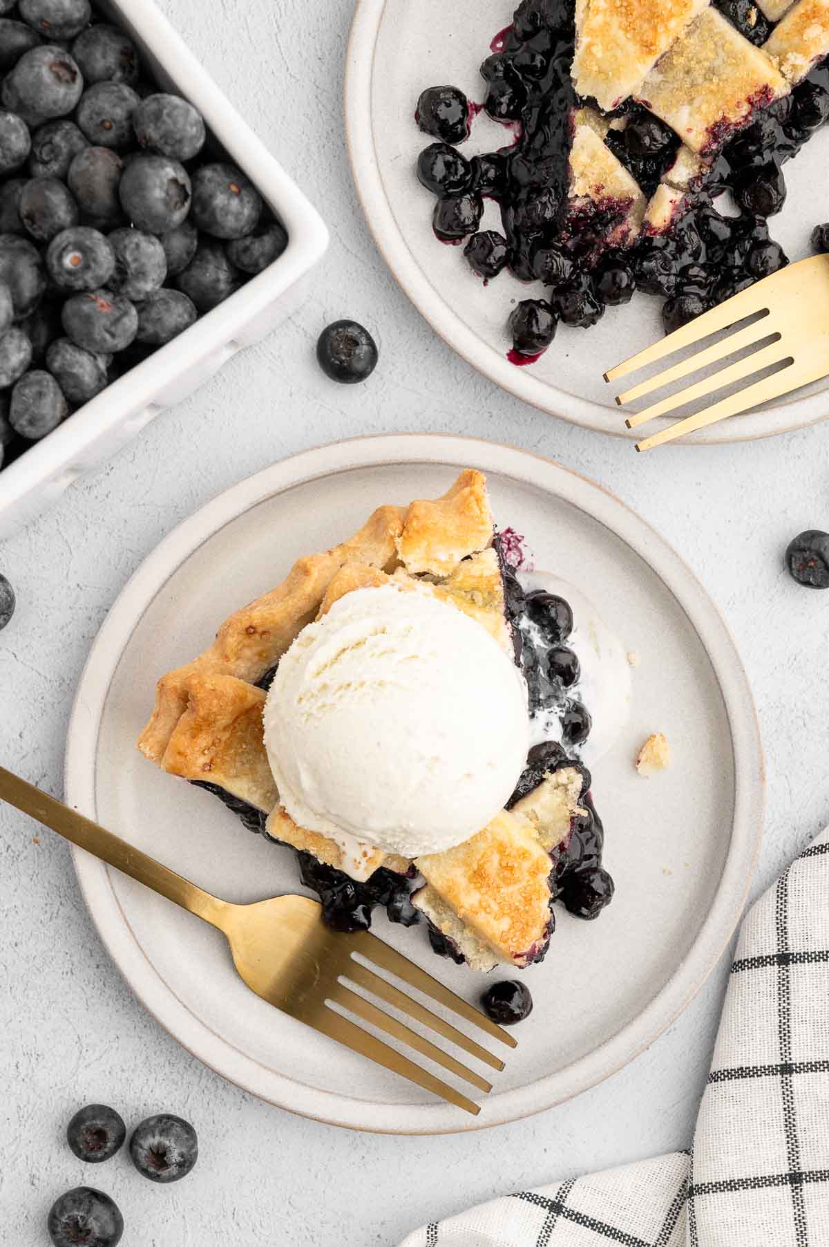 A slice of vegan blueberry pie on a plate with a scoop of vegan ice cream on top.