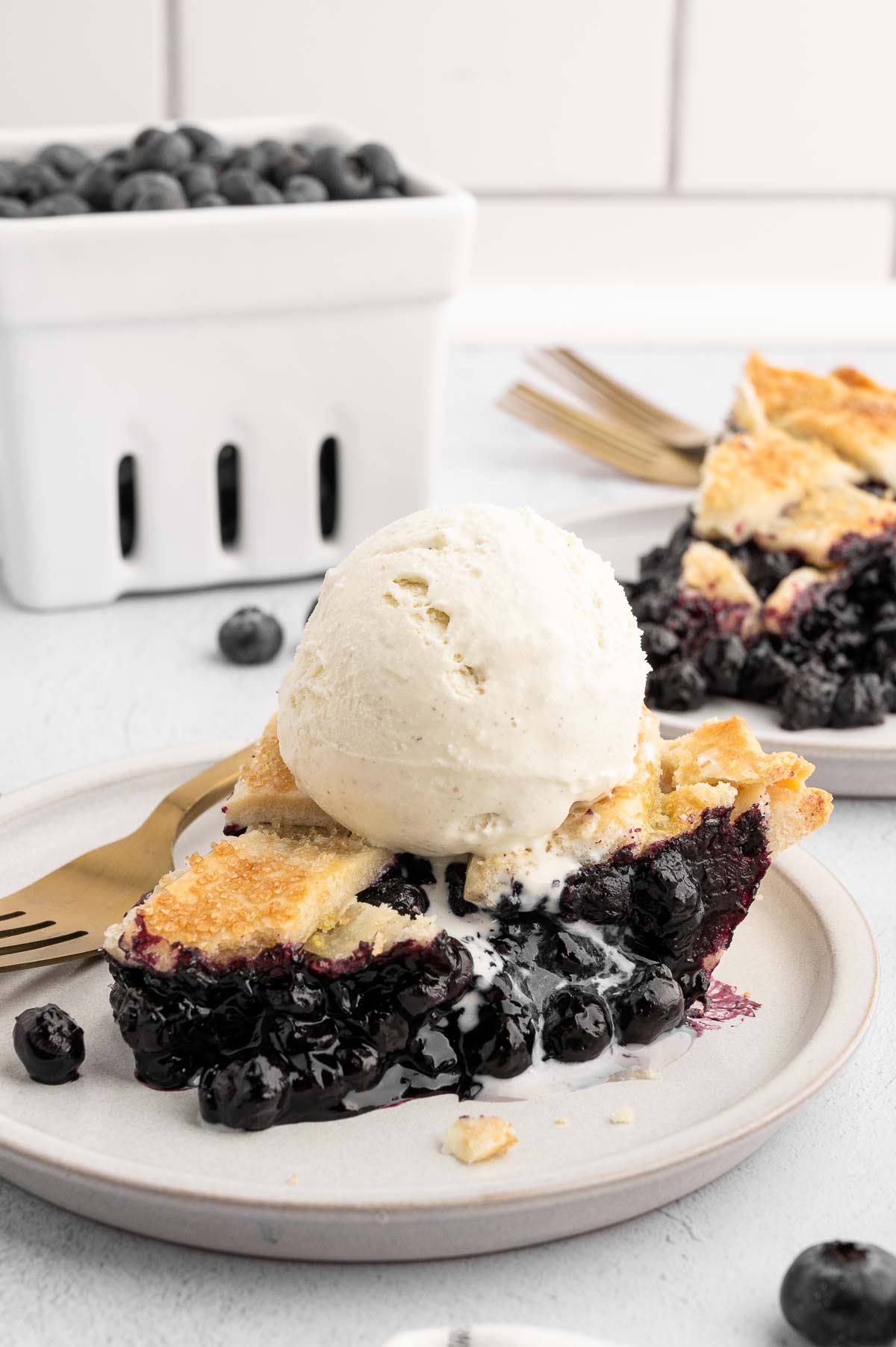 A slice of baked vegan blueberry pie with a big scoop of dairy-free vanilla ice cream on top. 