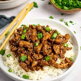 A plate of rice topped with vegan bulgogi, green onion and chopsticks resting on the side.