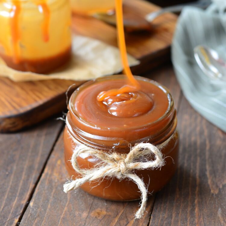 A small jar of vegan caramel sauce, with some caramel drizzling off a spoon into the jar.
