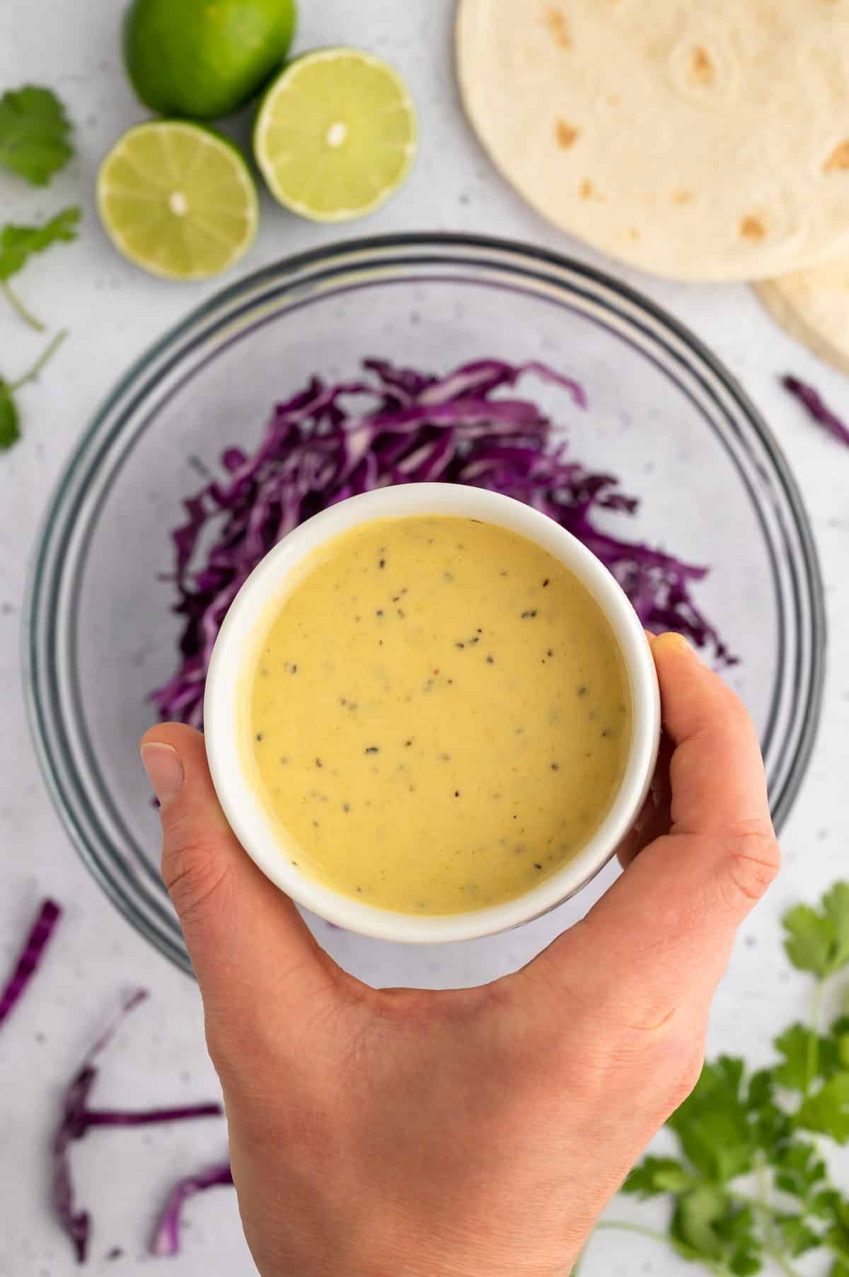 A small bowl of dressing over a larger bowl of shredded purple cauliflower.