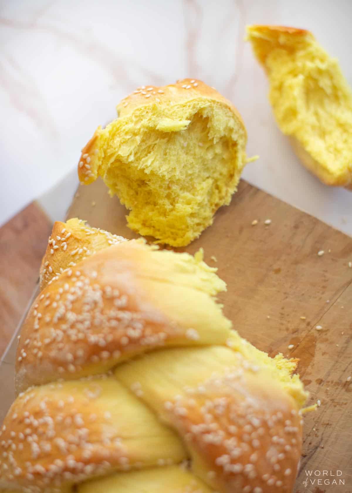 Vegan challah loaf with a couple pieces torn off, displaying the fluffy interior.