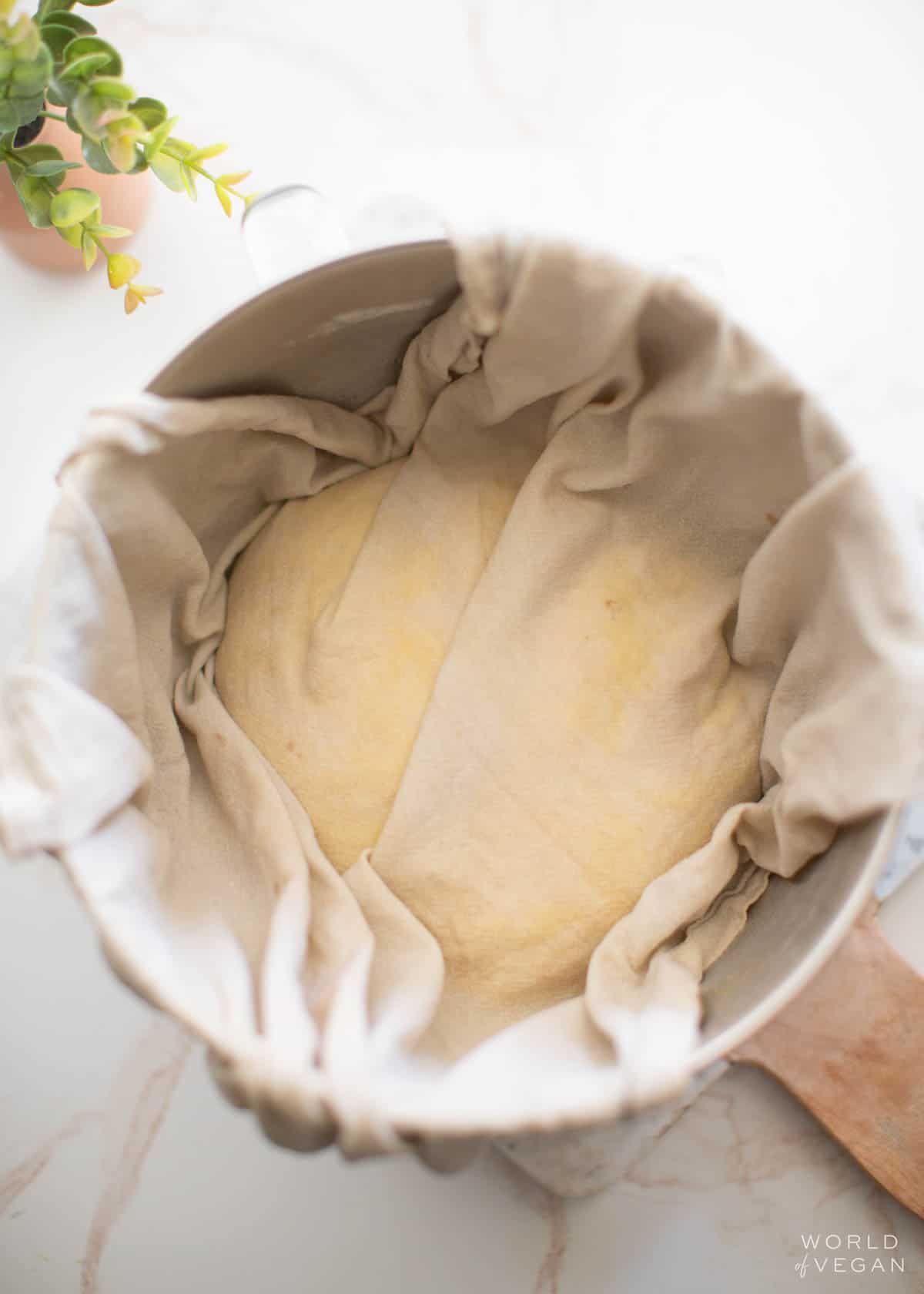 Vegan challah dough in a bowl, covered with a damp cloth while it rises.