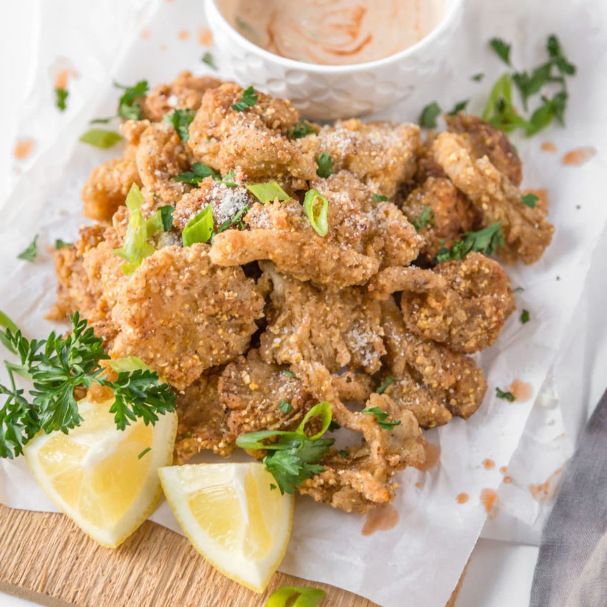 A pile of fried vegan chicken on a plate garnished with parsley and lemon.