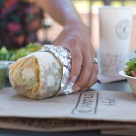 Woman Eating a Vegan Chipotle Burrito at the Outdoor Tables of the Restaurant