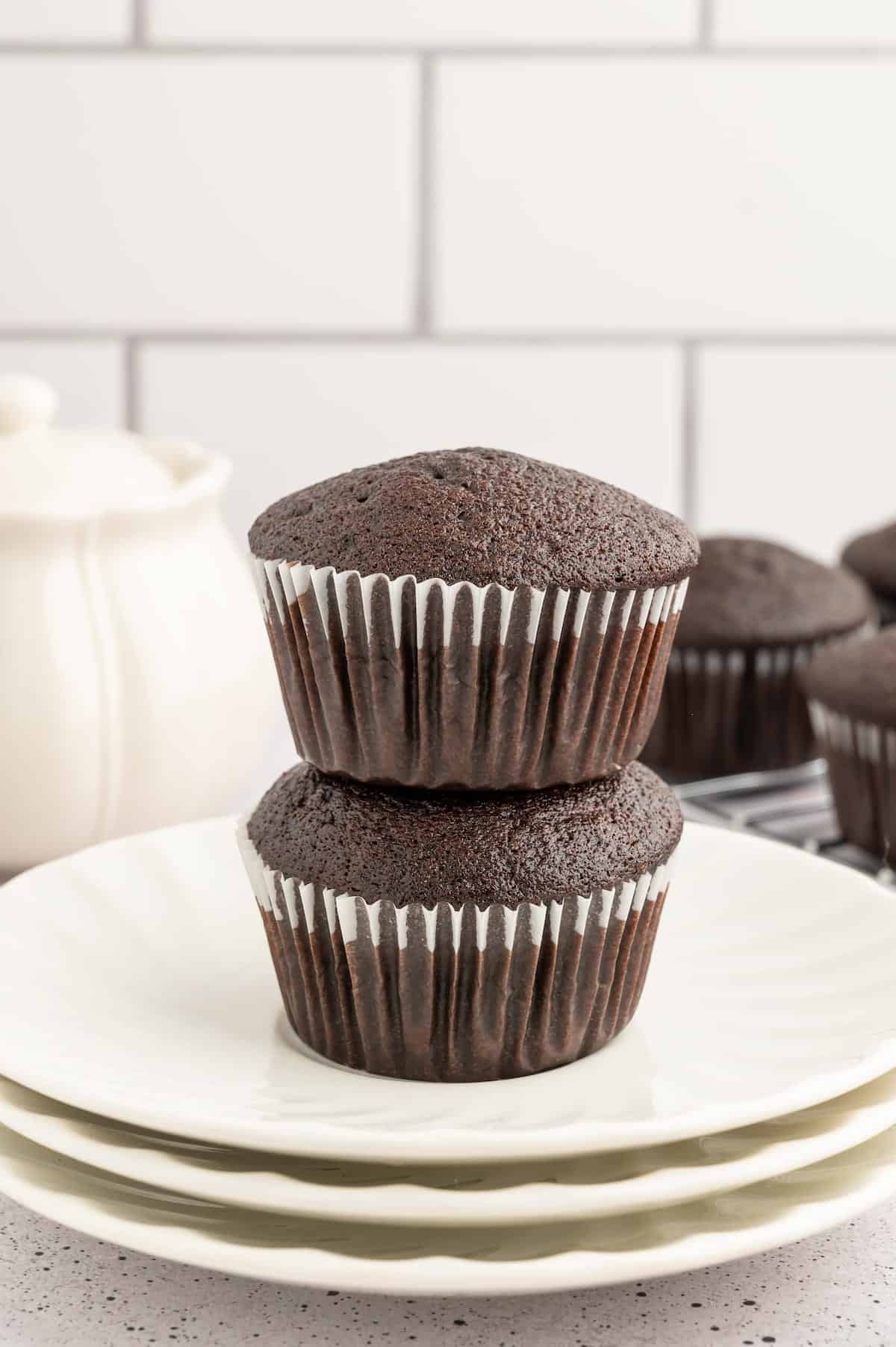 Two vegan chocolate cupcakes in liners stacked on a plate.