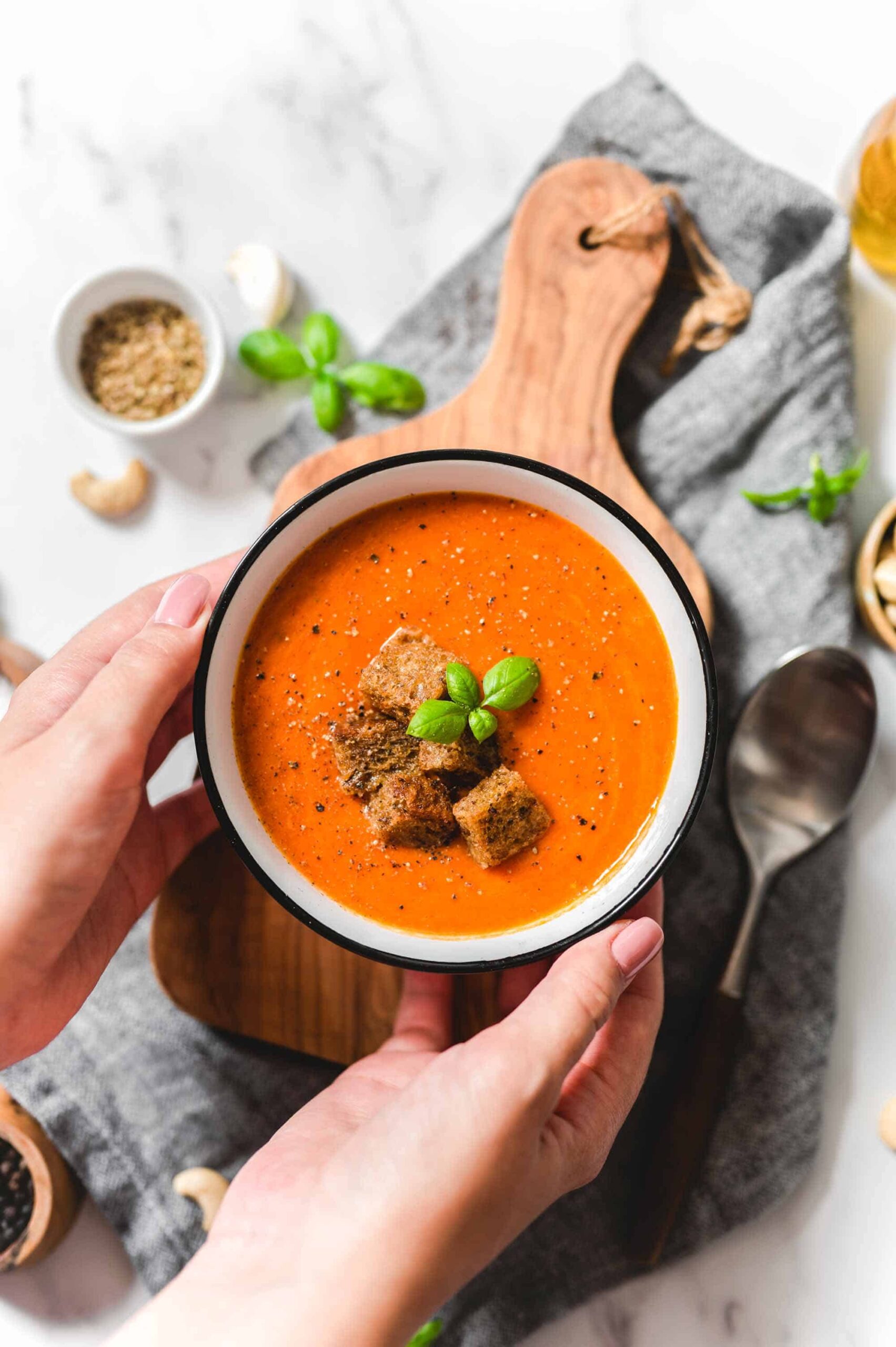 Creamy tomato soup from canned tomatoes in a bowl with croutons, basil leaves, cracked black pepper.