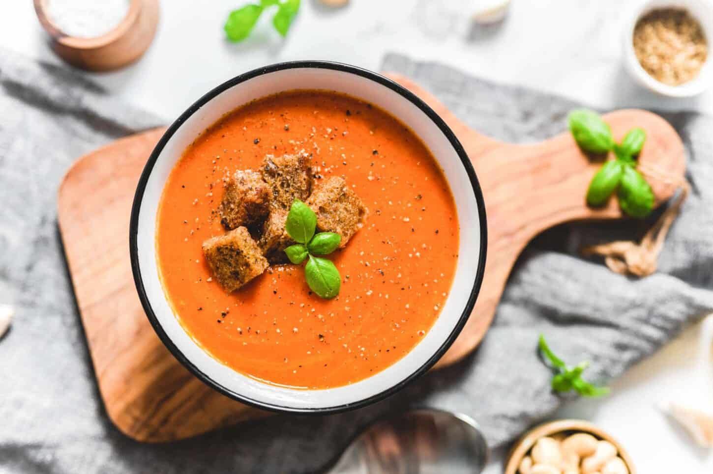 Easy Vegan Creamy Tomato Soup Garnished With Basil and Croutons on a Wood on a Cutting Board