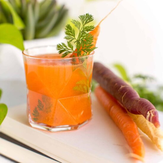 Orange carrot-infused moscow mule vegan cocktail with a carrot top sticking out.