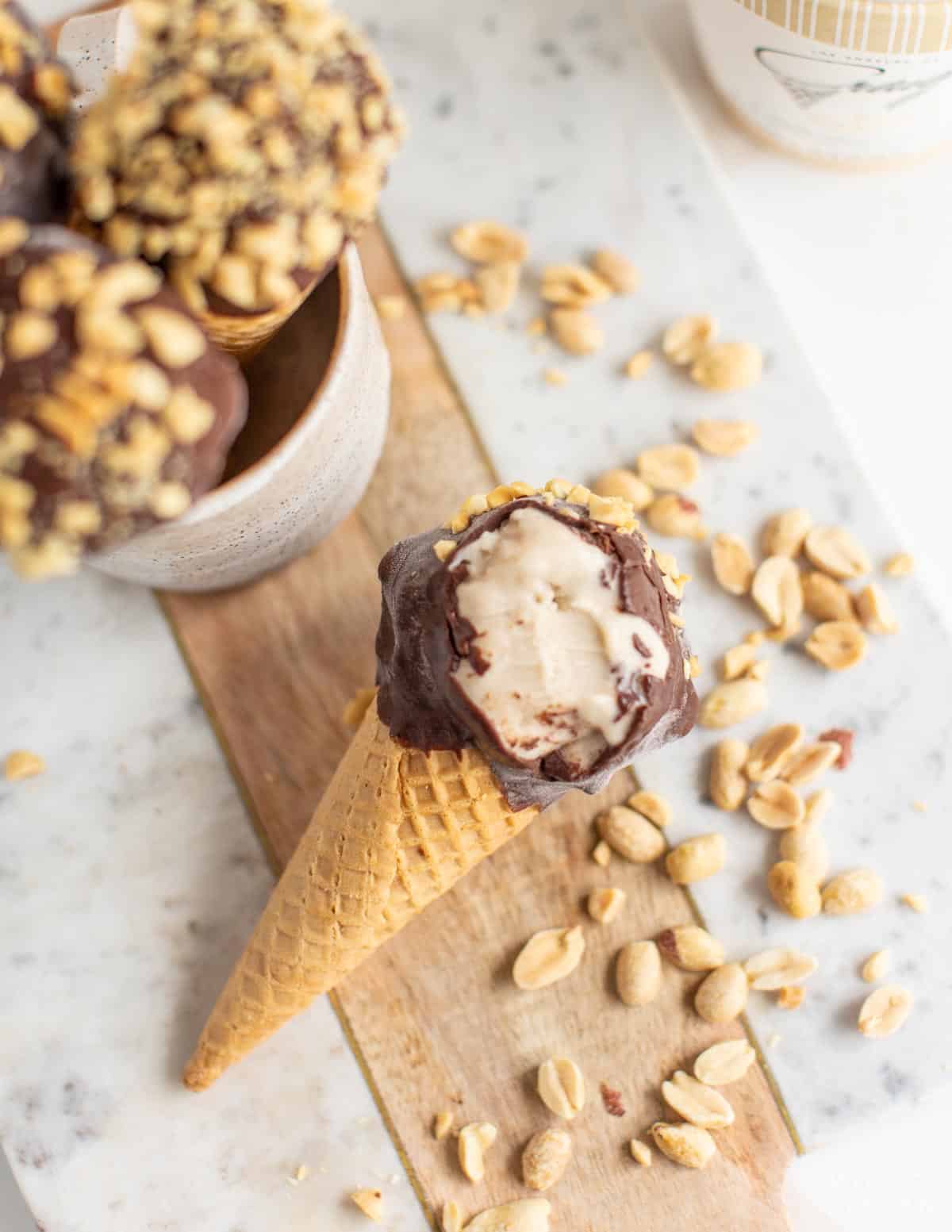 Delicious homemade vegan drumsticks on a counter with a bite out of one to expose the dairy-free vanilla ice cream inside. 