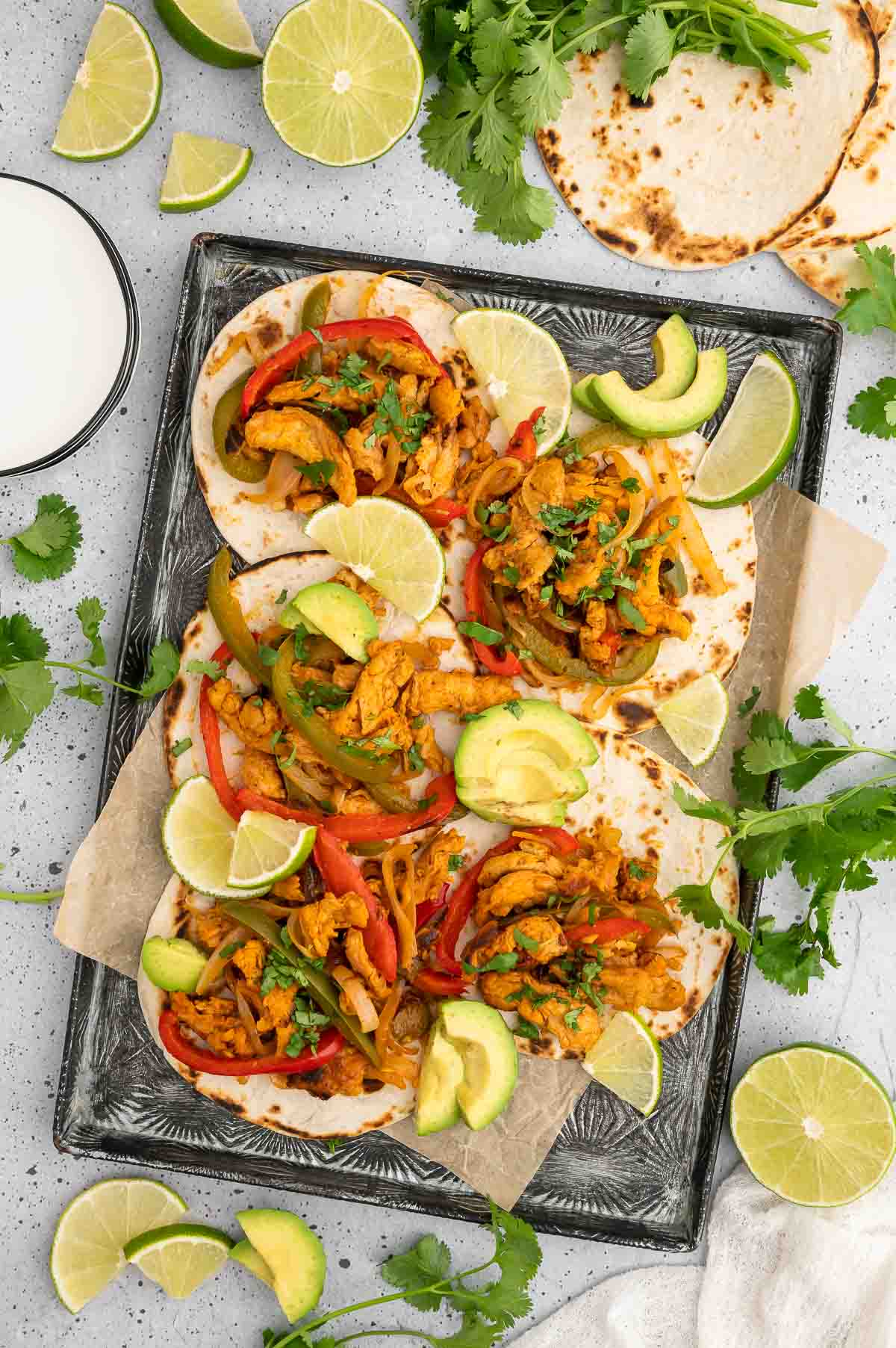 A sheet pan with vegan fajitas, garnished with limes and avocado.