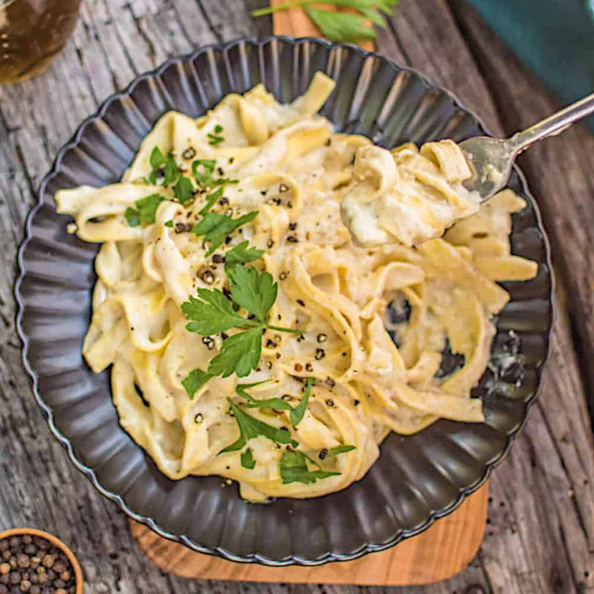 Dark grey plate full of vegan fettuccine alfredo and a fork twisted into the noodles.