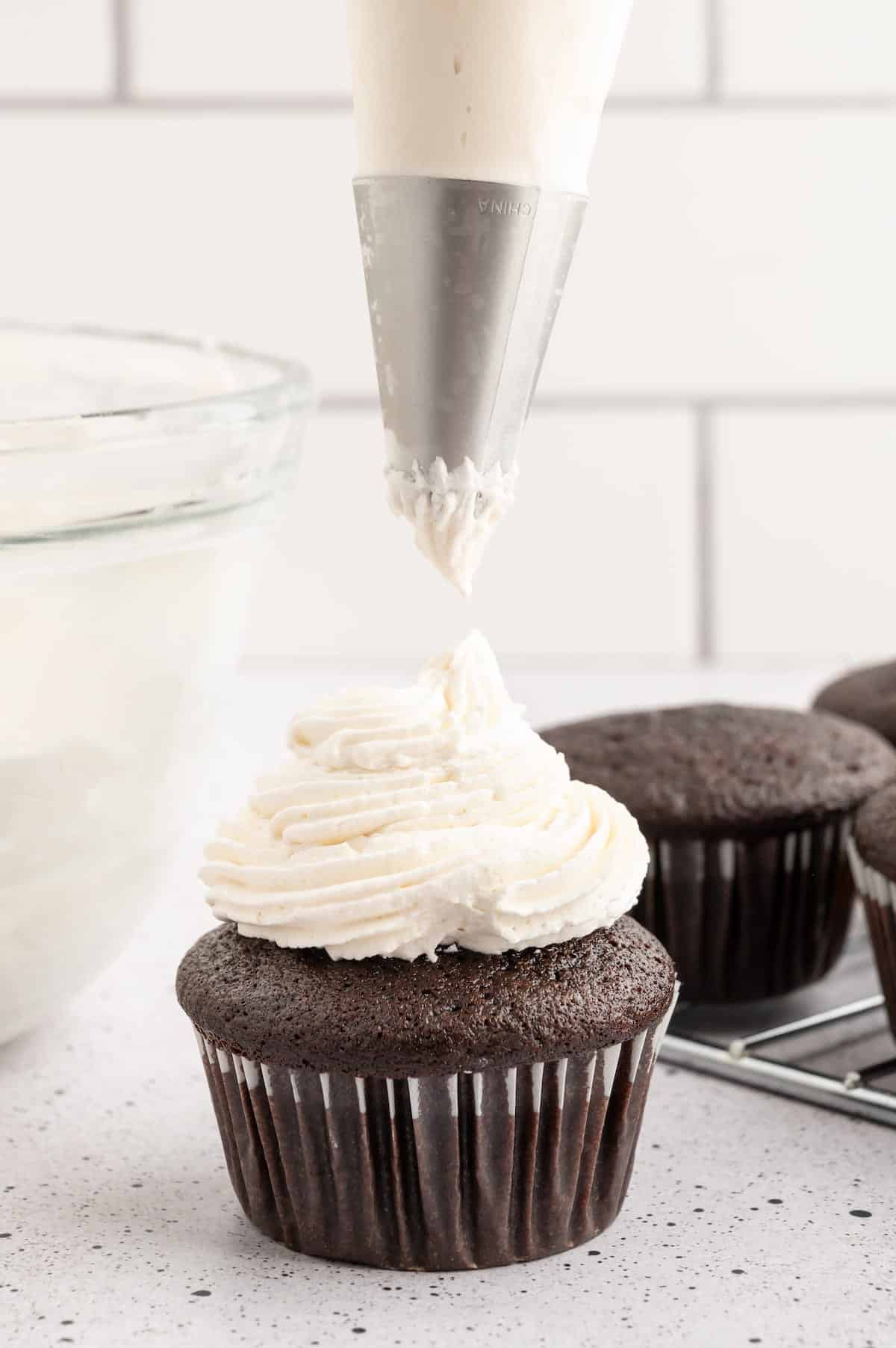 Vegan chocolate cupcake topped with buttercream frosting with piping bag hovering over top.