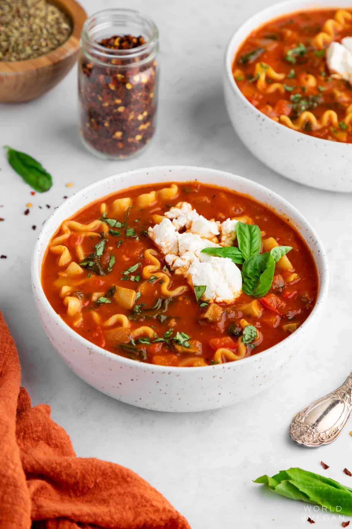 White dinner bowl with red lasagna soup sprinkled with red pepper flakes and basil. 