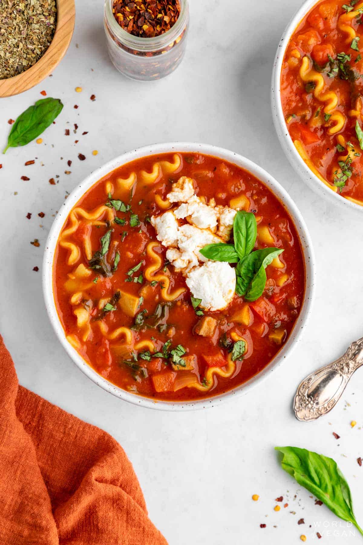 A bowl of red lasagna soup with tomato sauce, basil, noodles, and topped with dairy-free vegan ricotta cheese. 