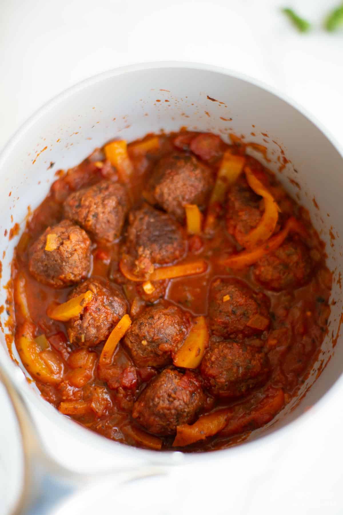 Veggie meatball simmering in pasta sauce in a pan. 