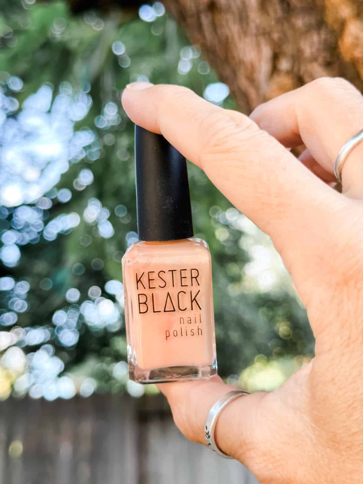 Holding a bottle of Kester Black nail polish in the shade light peach.