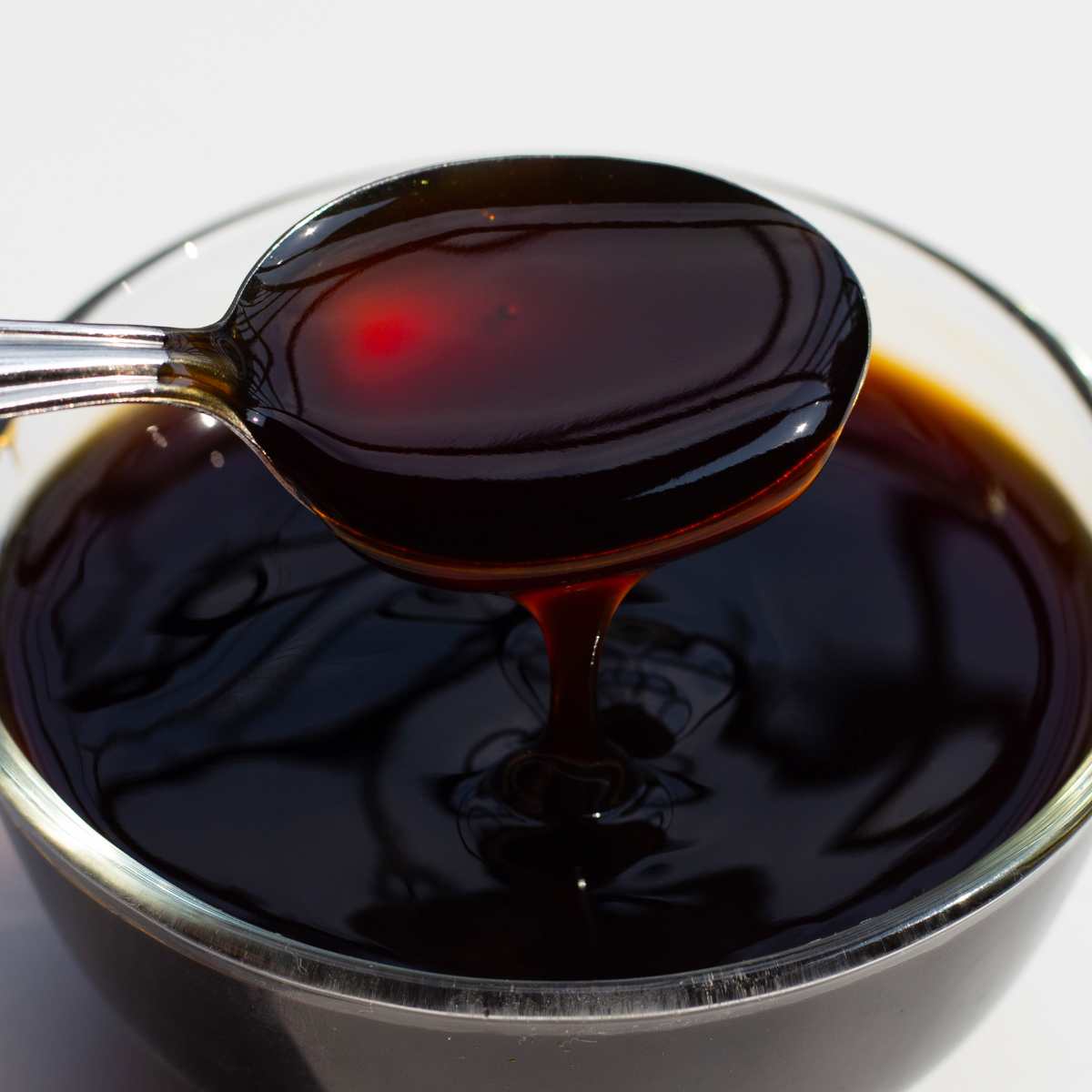 Vegan oyster sauce in a glass bowl with a spoon.