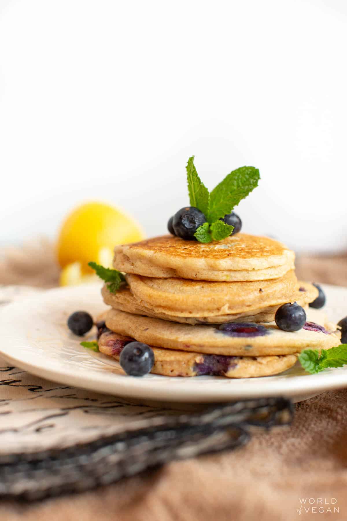 A small stack of vegan blueberry pancakes on a plate, topped with fresh blueberries.