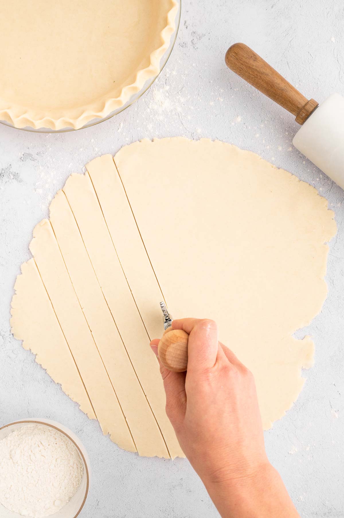 A hand using a pastry wheel on the pie crust dough to cut it into even strips.