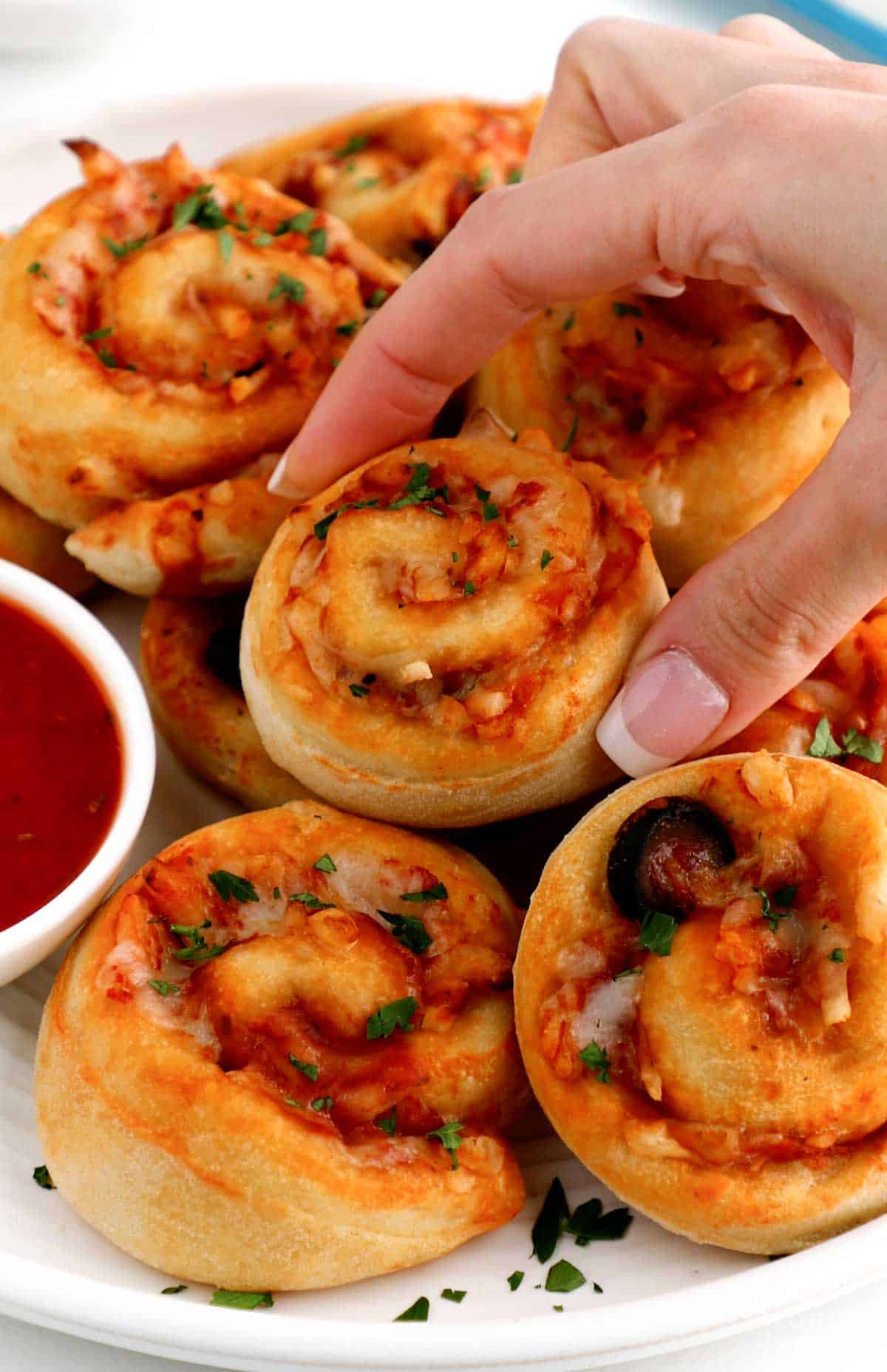 Woman picking up one of the cheesy vegan pizza rolls from the plate. 