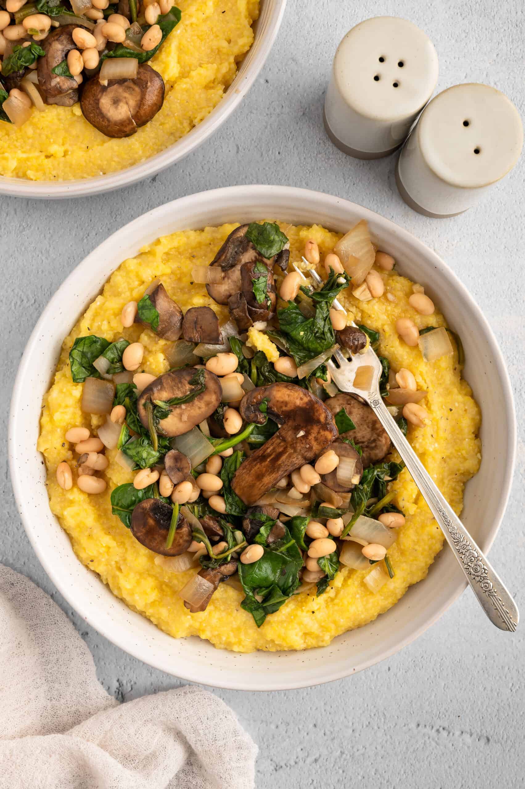 Bowl of creamy vegan polenta with sauteed mushrooms and greens.