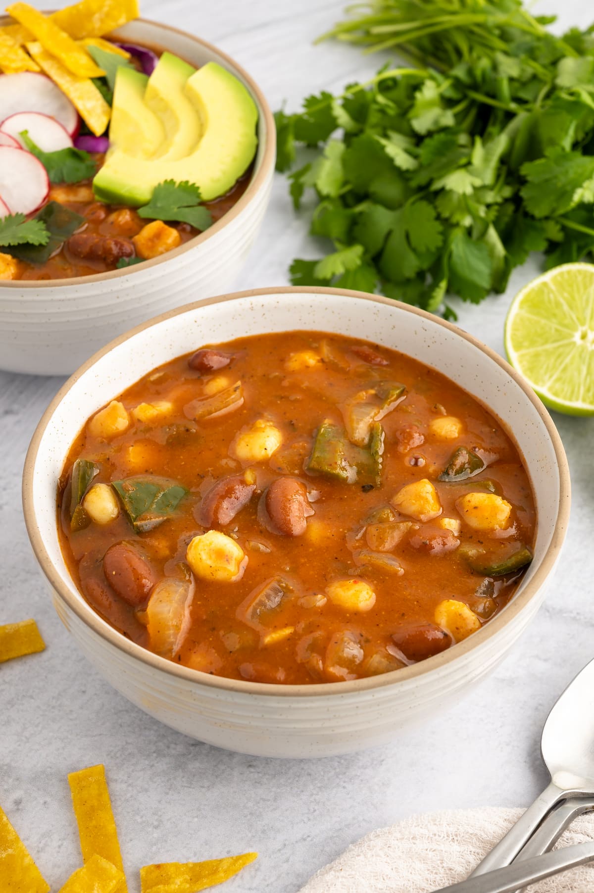 A bowl of vegan pozole. The front bowl is ungarnished and the back bowl is garnished.
