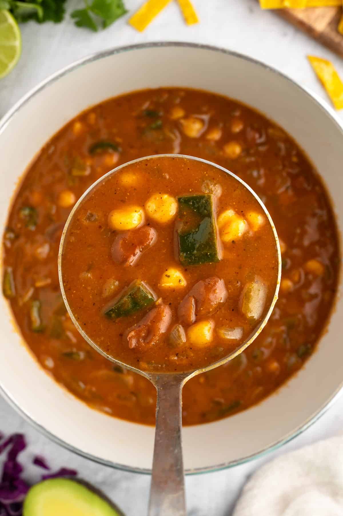 A ladle of vegan pozole being held over a white bowl.