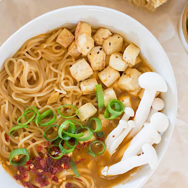 Best vegan ramen soup served in a white bowl with rice noodles topped with mushrooms, tofu, red pepper flakes