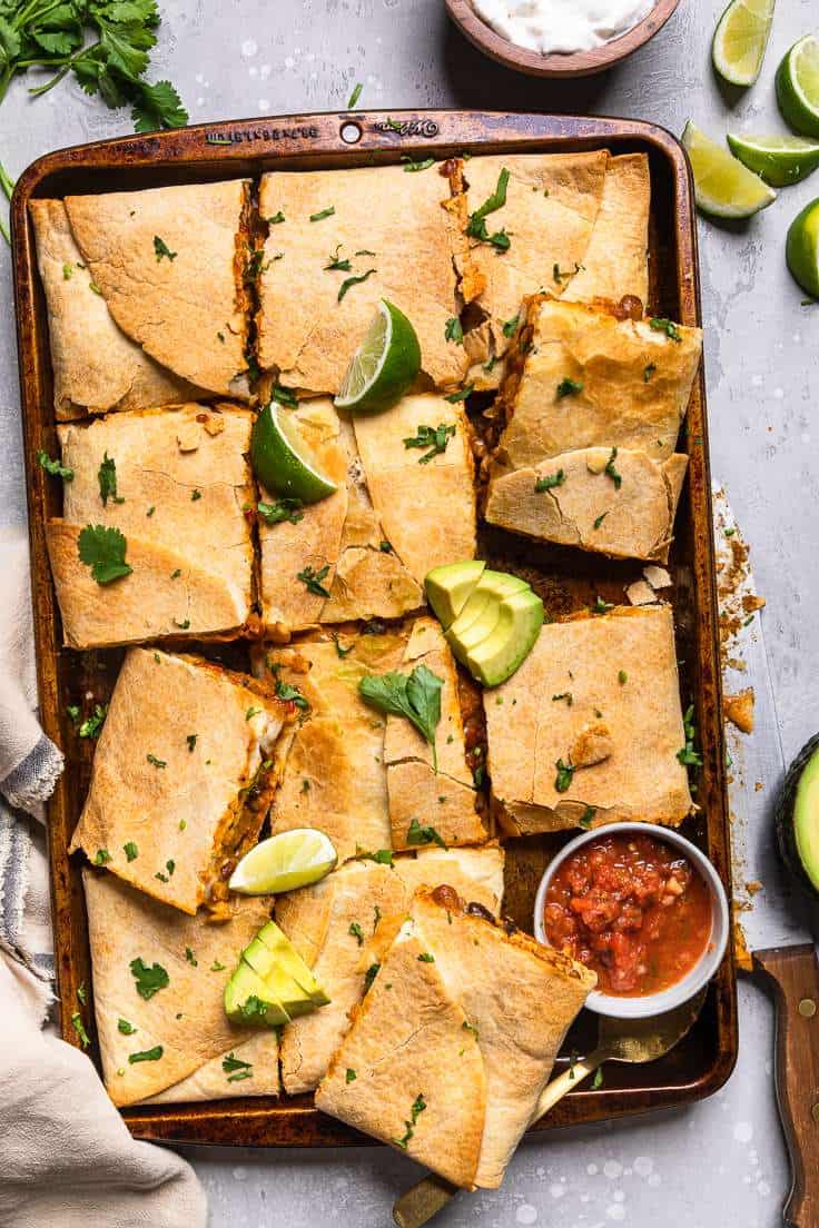 vegan sheet pan quesadillas garnished with limes, avocados, and a side of salsa