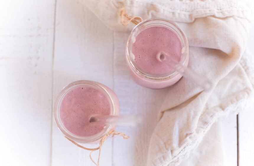 Two Mason Jars filled with Strawberries and Cream Smoothie and a cream colored cloth