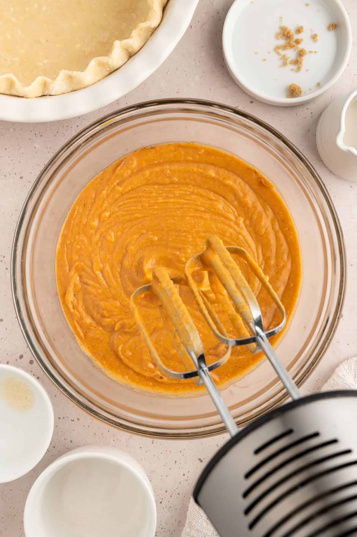 Vegan sweet potato pie batter in a bowl with an electric hand mixer hovering over.
