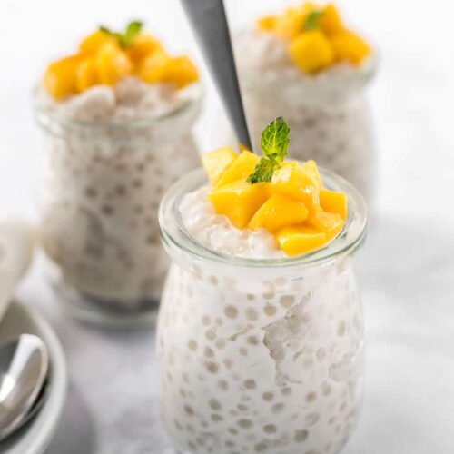 Easy Dairy-Free Tapioca Pudding in small glass jars topped with mango and a sprig of green mint.