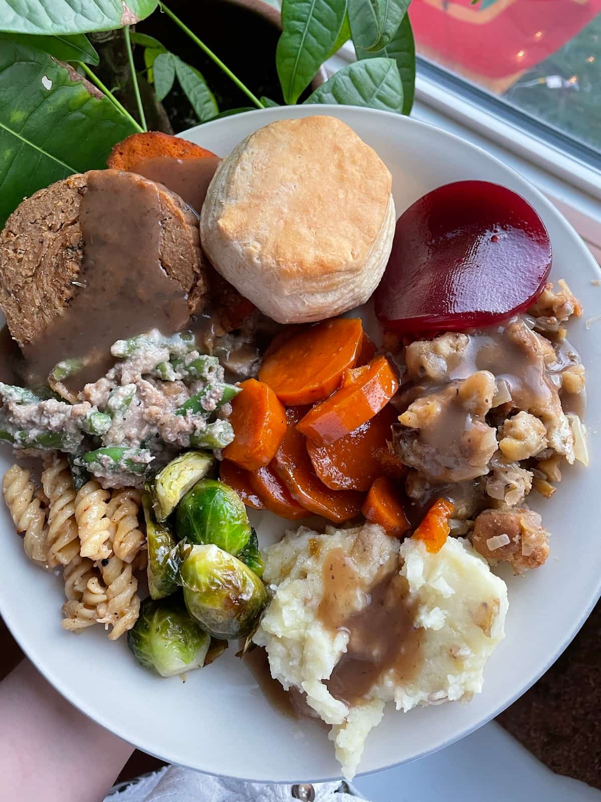 Vegan Thanksgiving plate of food including vegan turkey, mashed potato, roasted veggies, cranberry sauce, and a biscuit.
