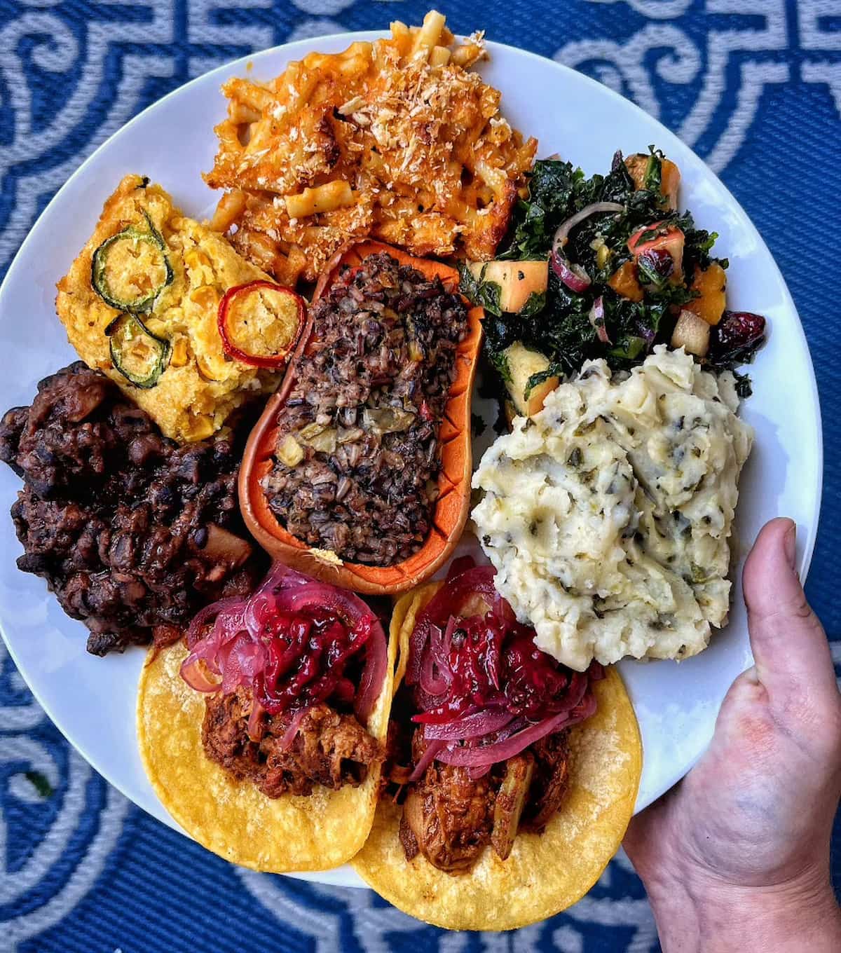 A plate of vegan Thanksgiving food including mashed potatoes, stuffed butternut squash, tacos, and various casseroles and salad.