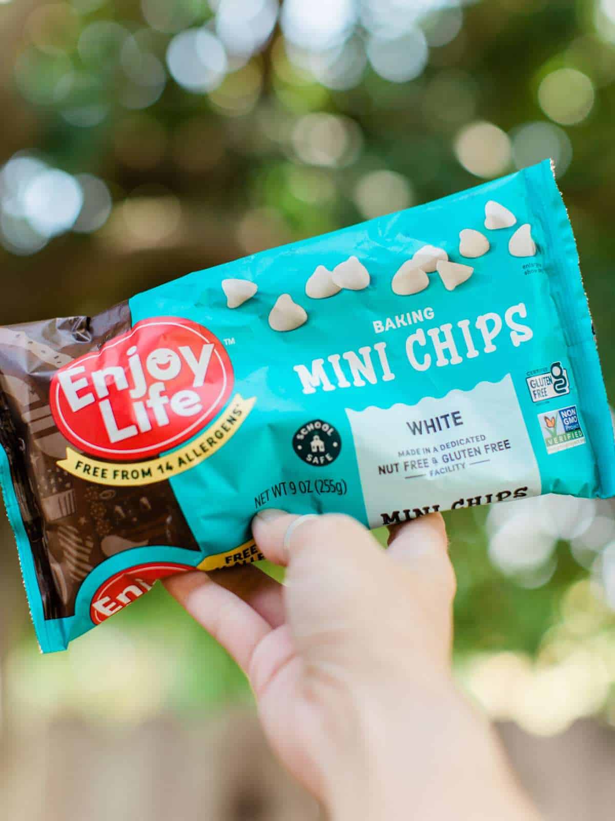 Woman's hand holding out a bag of vegan white chocolate chips from the brand Enjoy Life. 