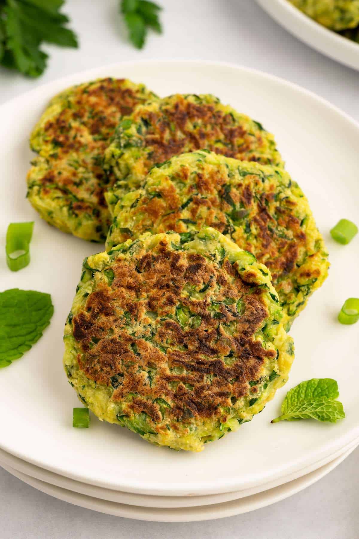 Four vegan zucchini fritters overlapping in a line on a plate.