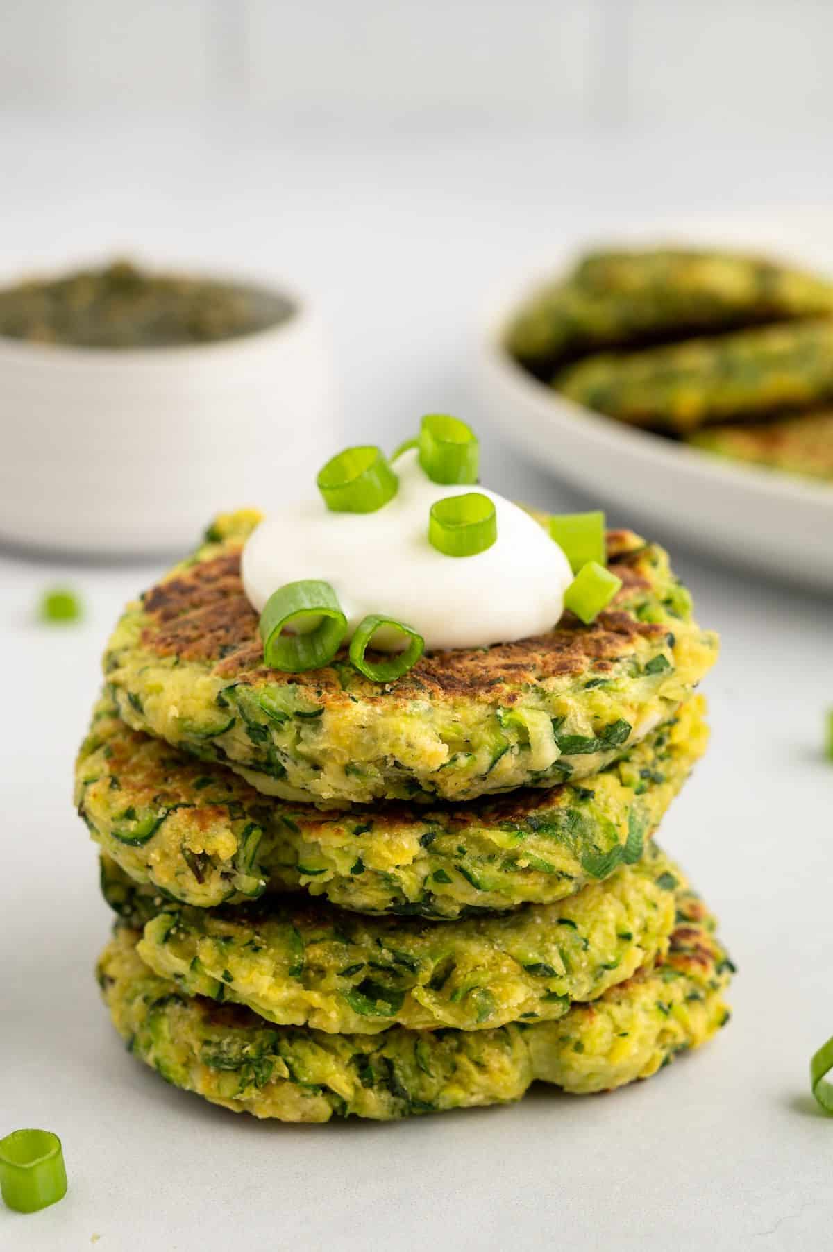 A stack of vegan zucchini fritters with vegan sour cream and chives on top.