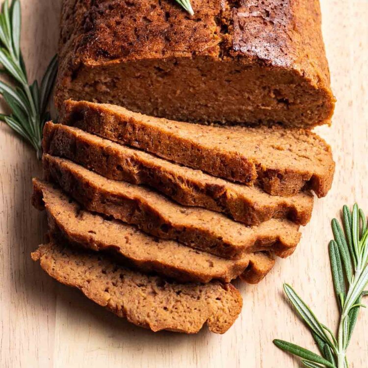 Sliced vegetarian roast on a cutting board surrounded by fresh rosemary herbs.