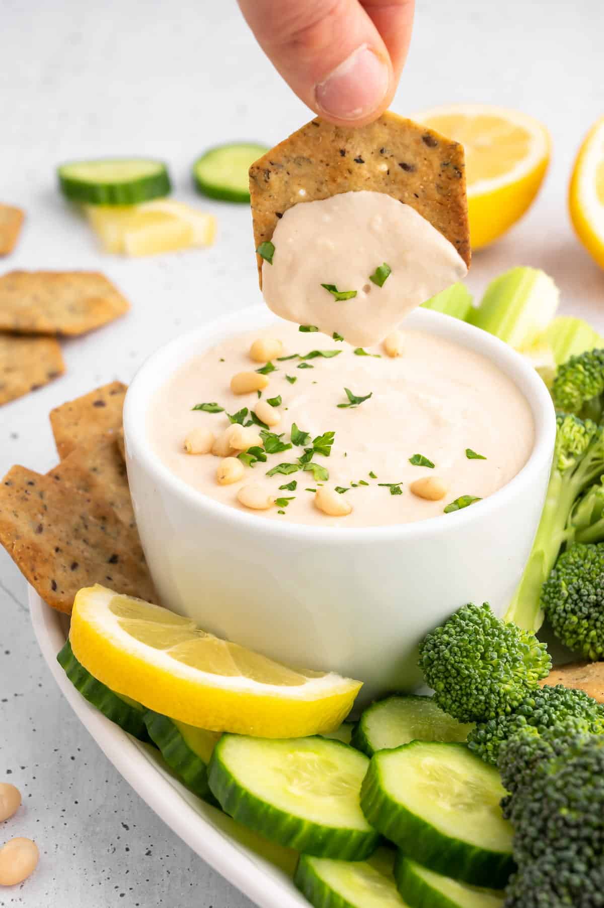 A cracker being dipped in white bean hummus.